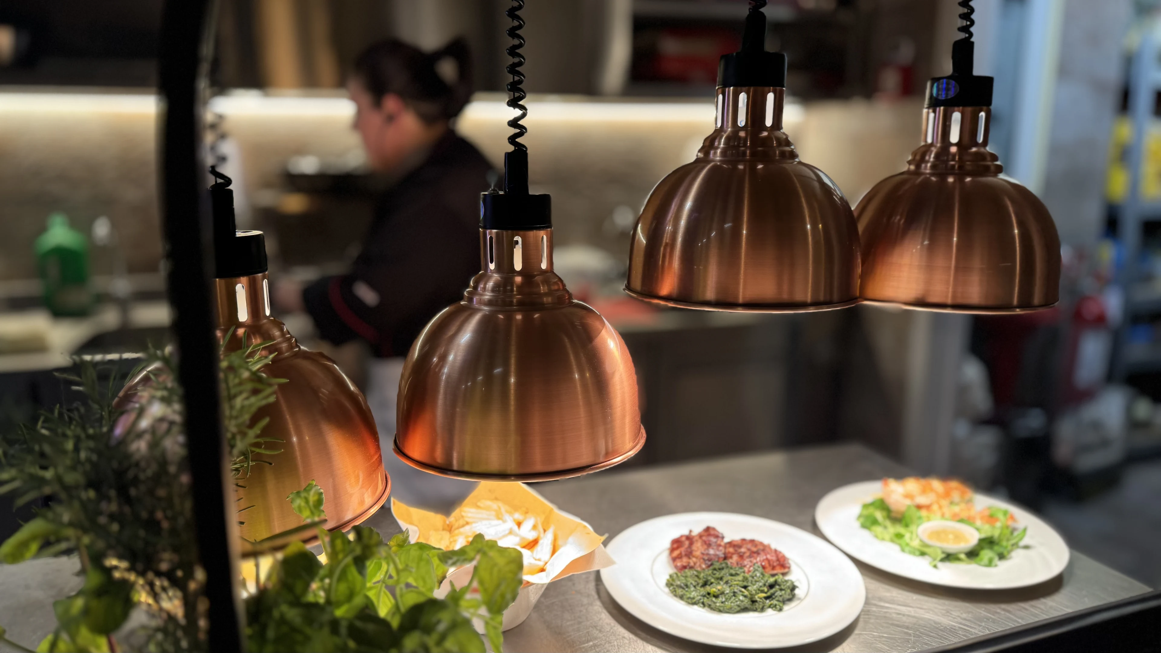 Lampade riscaldanti in rame sopra i piatti pronti al pass della cucina a vista della Hosteria La Togata